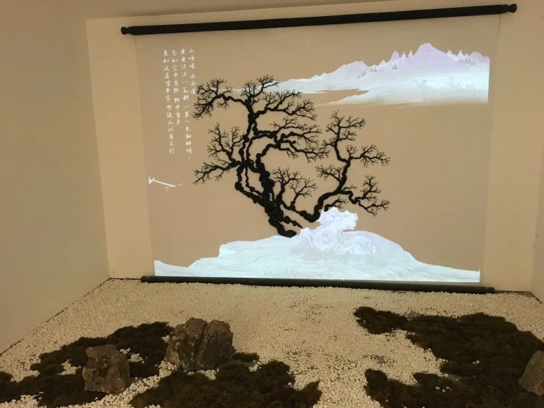 元禾大千艺术品有限公司室内艺术造型封面图,白色山水投影背景与黑色枯枝树形装置结合,前景铺设白石、苔藓与山石,呈现东方山水意境与当代艺术空间融合